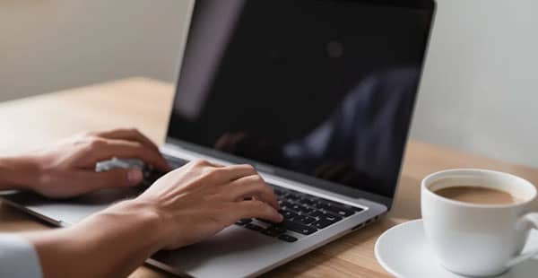 The image shows a person's hands typing on a laptop computer at a desk, with a coffee cup placed nearby, creating a cozy workspace atmosphere. This setting is ideal for exploring online casinos that offer low minimum deposits and attractive welcome bonuses.